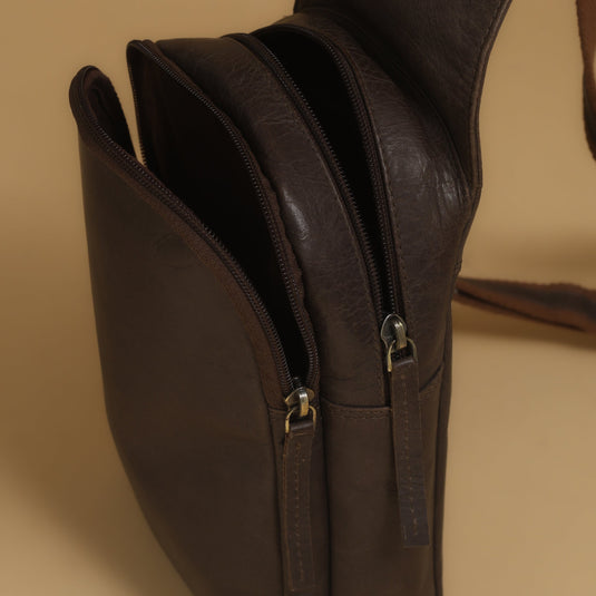 Brown eco-leather body bag with dual zip compartments on beige background