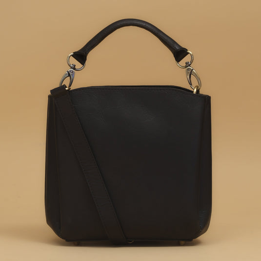 Black eco-leather mini crossbody bag with adjustable strap and gold-tone hardware on beige background