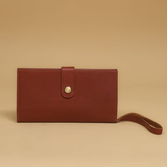 brown eco-leather wrist purse with button closure and strap on beige background